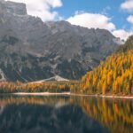 Stunning autumn landscape of Trentino mountains reflected in a serene lake, showcasing vivid fall colors.