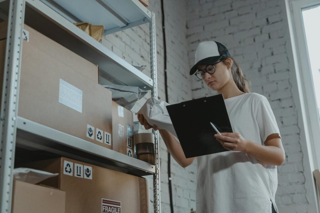 Warehouse worker organizing packages on shelf with clipboard.