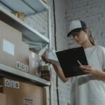 Warehouse worker organizing packages on shelf with clipboard.