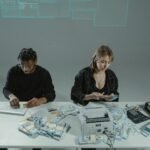 Two people counting money at a desk with computers and cash equipment.